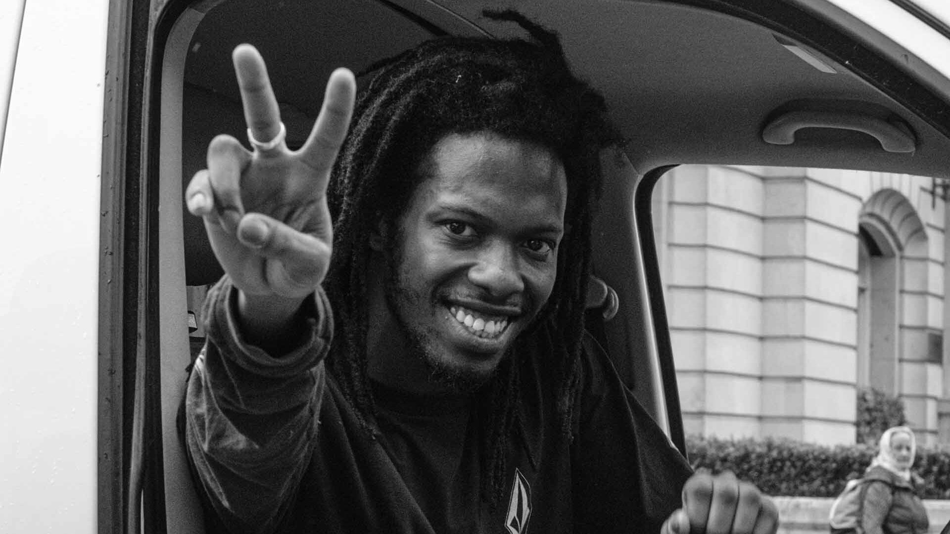 black man in a van smiling with empathy and showing the peace sign with his hand