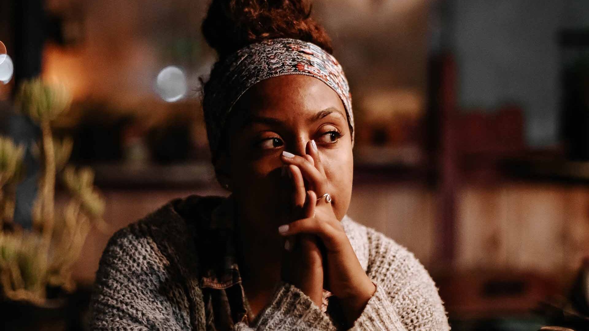 black woman sitting down. her hands in front of her face. she has a worried look on her face.