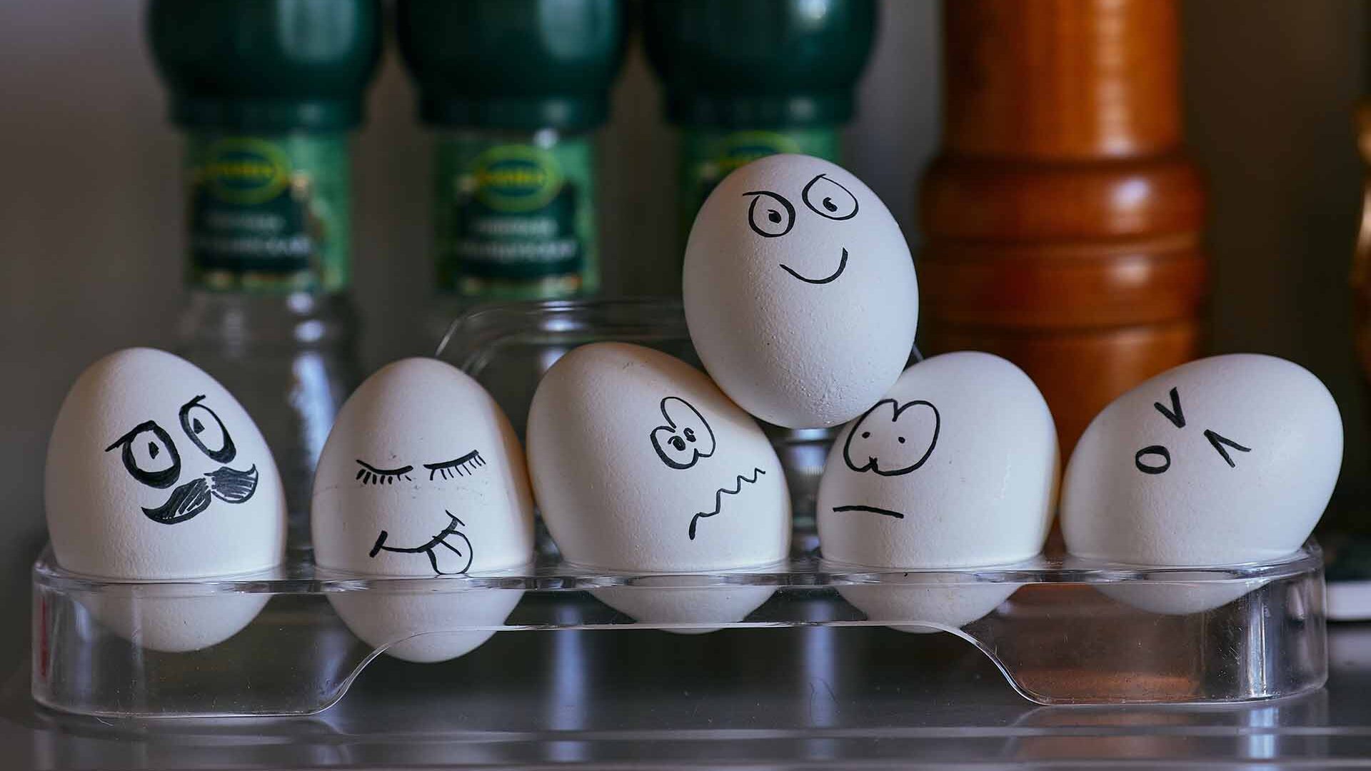six white eggs sitting on a shelf with faces drawn on them.