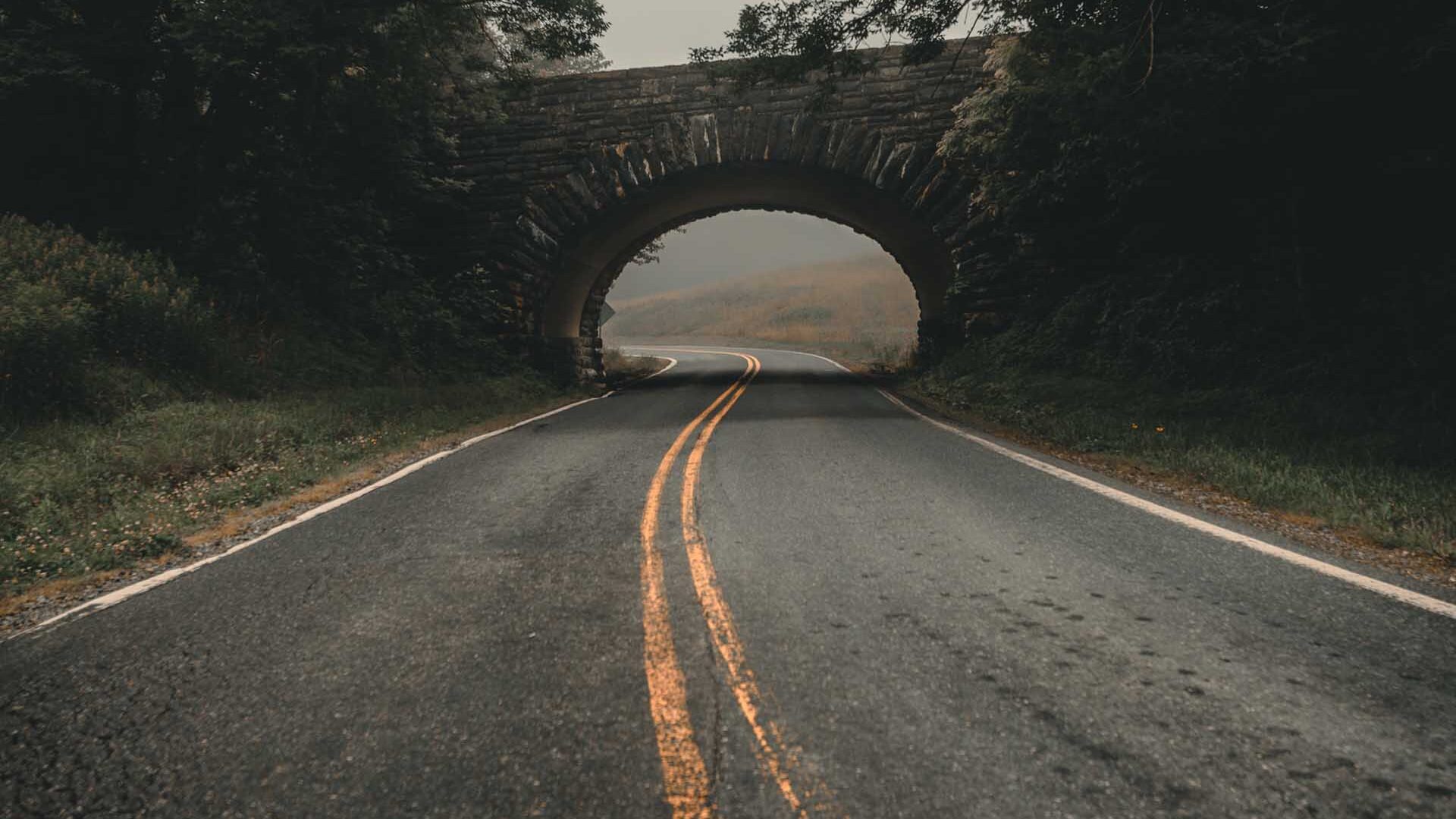 empty-road-under-stone-bridge paved country road disappears into distance. there is an arched stone bridge over the road.