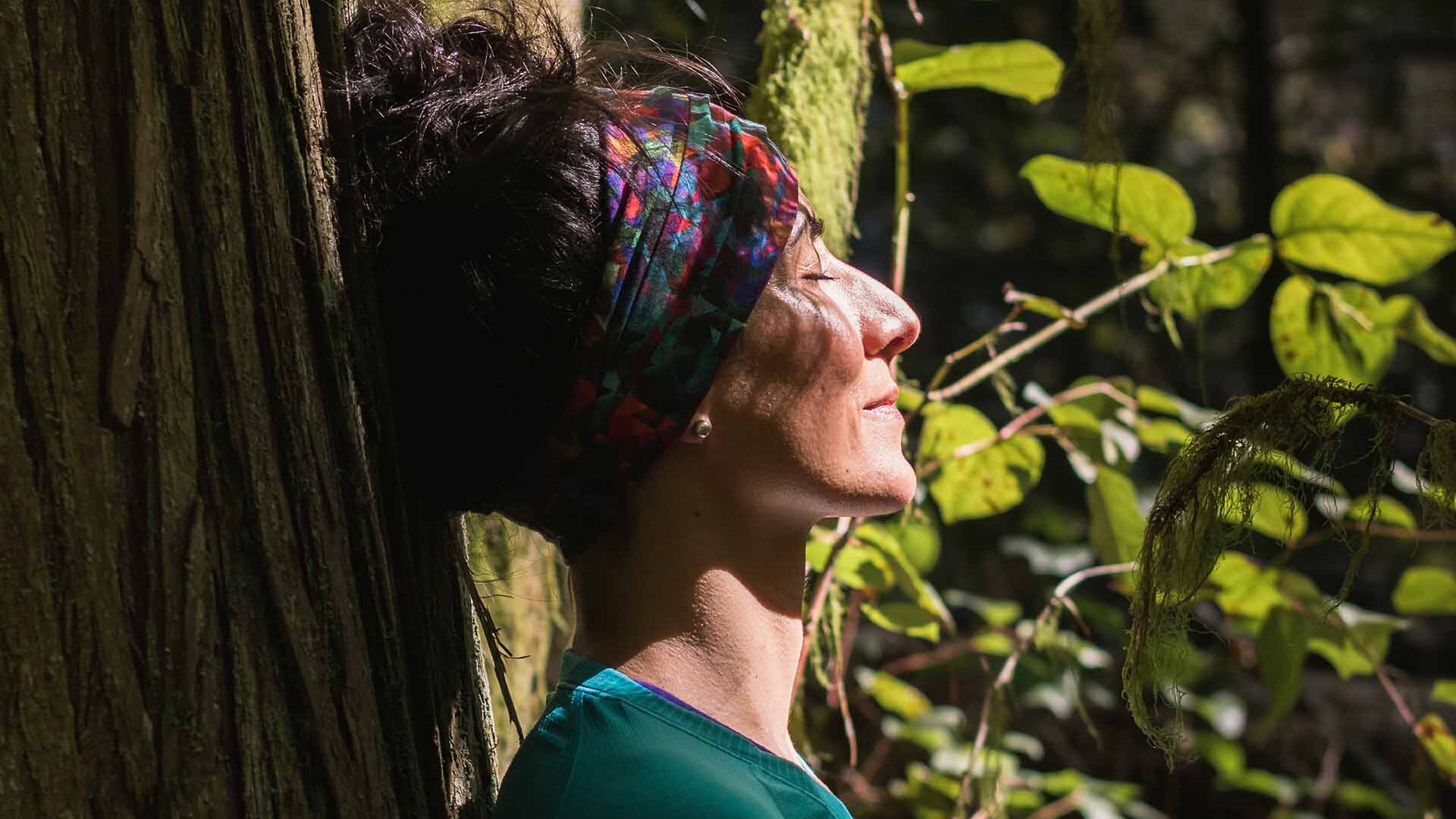 middle aged woman in the forest leaning her head against a tree in a peaceful pose